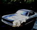 1968 Ford Mustang - A white 1968 Ford Mustang convertible with racing stripes on the hood is parked outside.