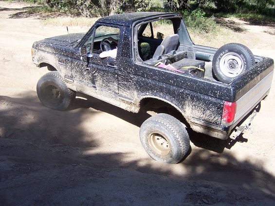 Black Ford Bronco covered in mud, driving on a dirt road
