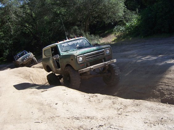 Green off-road SUV with white roof driving on a dirt trail, front view