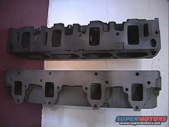 Two engine cylinder heads are shown, one above the other. The top one is darker and has a more complex shape