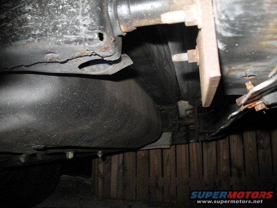 Vehicle underbody with fuel tank and rusted frame components, supported by wooden blocks