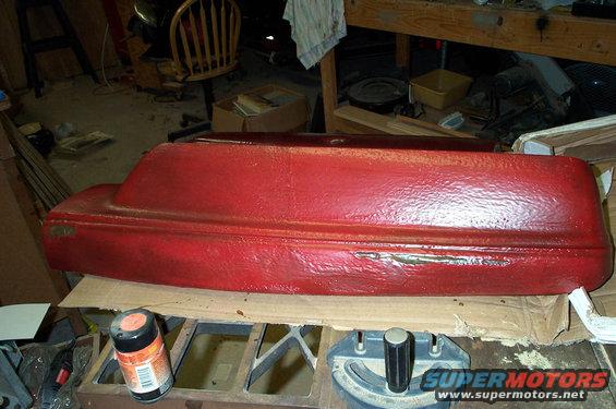 red painted car part on a workbench with a spray can