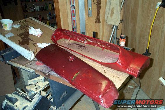 Red vehicle fender and grille assembly on a workbench with tools and supplies