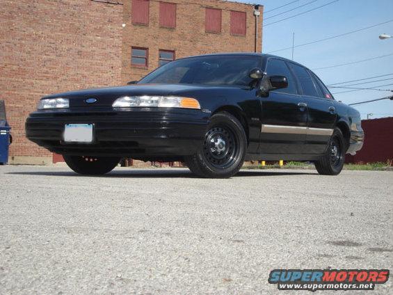 Black 1992 Ford Crown Victoria sedan parked on asphalt, front 3/4 view, brick building in background