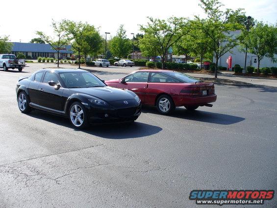 Red coupe parked on asphalt, rear 3/4 view. Spoiler on trunk, alloy wheels