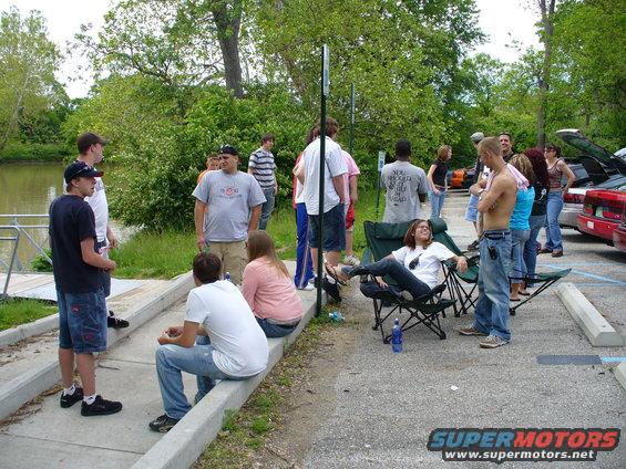 People gathered outdoors by a water feature, some sitting in chairs, others standing