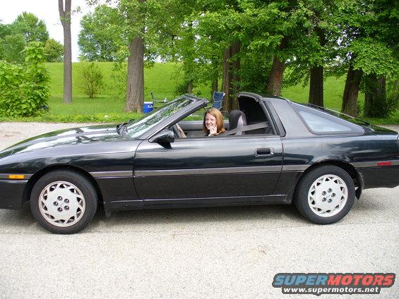 Black convertible sports car with a woman driving, side view. The car has a removable targa top