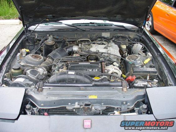 Engine bay with 7M-GE engine and orange car in background