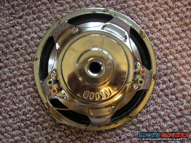 Round car audio subwoofer with chrome accents and "600W" text, resting on carpet
