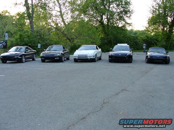 Five cars parked in a lot, including a black 1991 Ford Probe on the far left