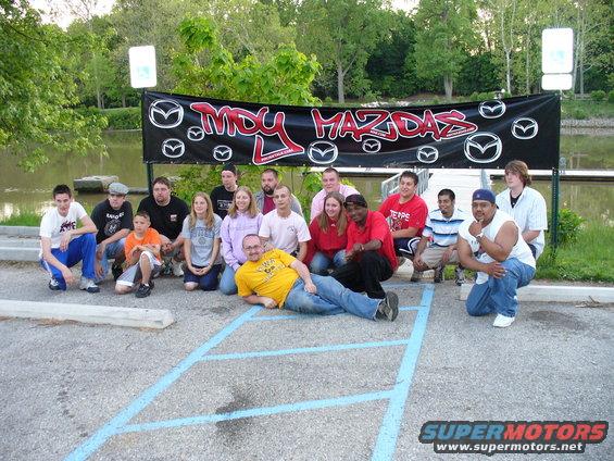 Group of people in front of a black banner with 'MDY MAZDAS' logo and Mazda emblems