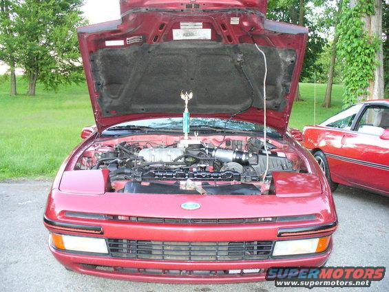 Red 1991 Ford Probe with hood open showing engine and a trophy. Another red Probe is parked next to it
