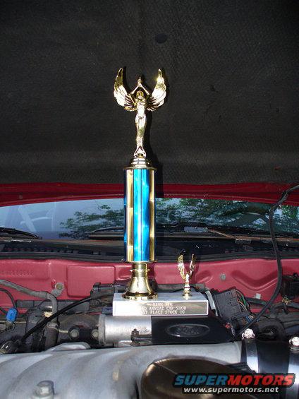 Trophy on red car engine bay, with "BAMM 06 3rd ANNUAL CAR SHOW 1ST PLACE STOCK 10" plaque