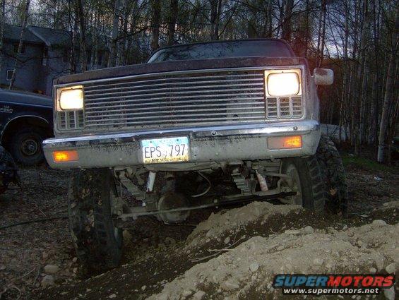 Front view of a lifted 1980s pickup truck with a chrome grille and headlights on