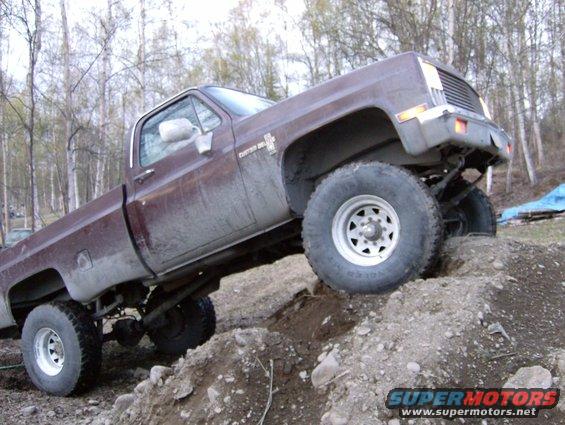 Brown pickup truck climbing over dirt mounds. Has 'CHEVROLET' badge on fender