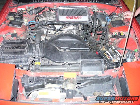 Engine bay of a red Mazda, showing the 13B intercooled turbo II engine, air intake, and battery