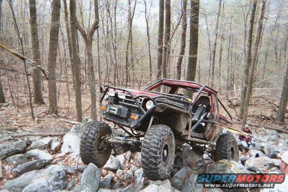 Off-road buggy with large tires navigating a rocky trail in the woods. Winch on front bumper