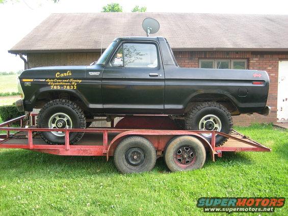Black 1978 Ford Bronco on a red trailer, side view. Text on door reads 'Carl's Auto Care and Towing'
