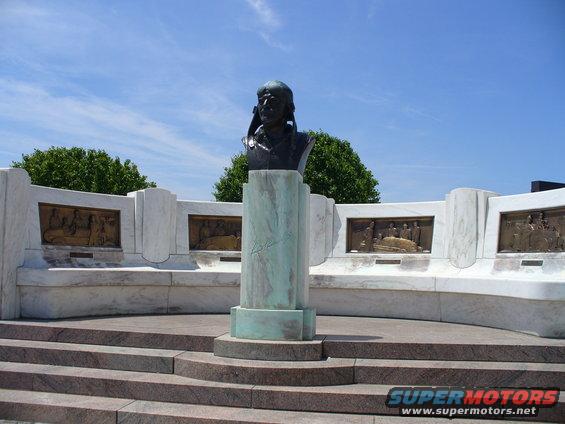 Monument with a bust on a marble pedestal, surrounded by a curved marble wall with relief panels