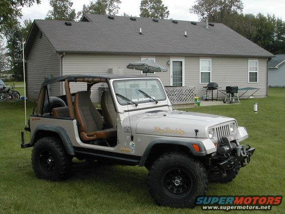 Silver Jeep Wrangler with "Big Daddy" on the hood, parked on grass in front of a house