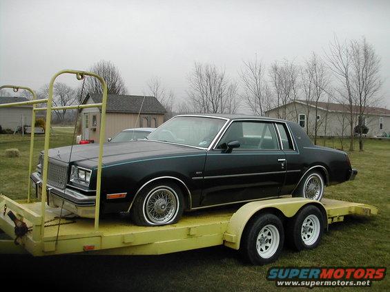 Black coupe with wire wheels on a yellow trailer