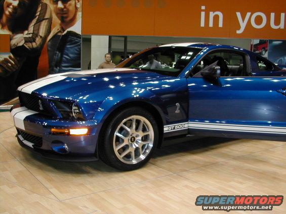 Blue Ford Mustang GT500 with white racing stripes, driver's door open