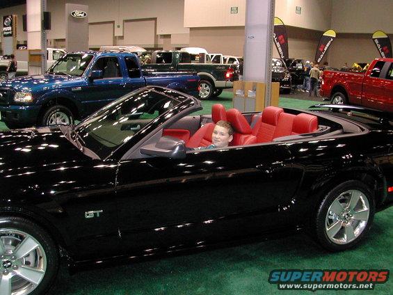 Black convertible with red interior, a young boy sits in the driver's seat. GT badge visible on fender