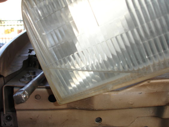 Close-up of a clear plastic headlight lens with vertical fluting, showing mounting hardware underneath
