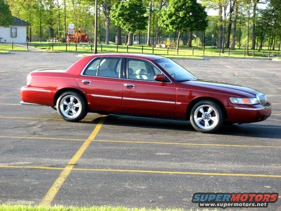 Red 2000 Mercury Grand Marquis parked in a lot with trees and a playground in the background