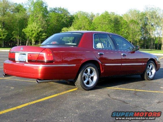 Red sedan parked in a lot, trees in background. It's a 2000 Mercury Grand Marquis