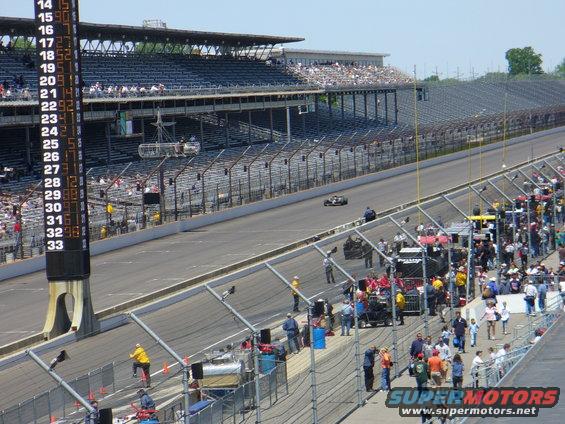 Race car on track with grandstands and pit crew visible
