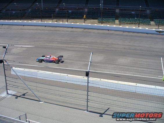 Open-wheel race car with colorful livery on a race track, viewed from the side
