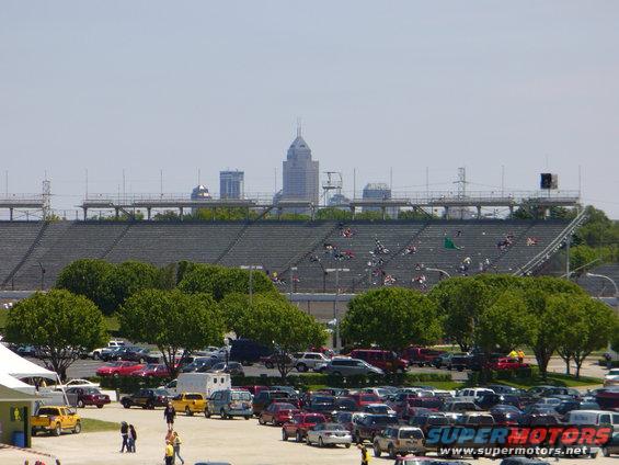 Parking lot full of cars with a stadium and city skyline behind