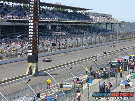 Race cars on a track with grandstands and a scoreboard