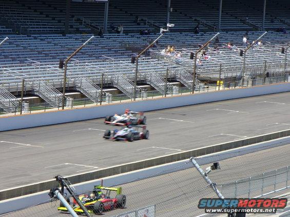 Race cars on a track with grandstands in the background