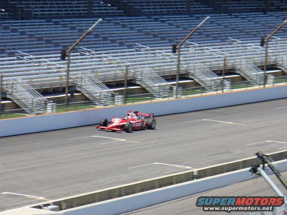 Red IndyCar racing on a track with empty grandstands in the background