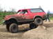 1989 Ford Bronco - A red Ford Bronco navigates an off-road course with a person watching in the background.