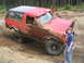 1989 Ford Bronco - A red SUV is shown off-roading on a muddy trail with trees in the background.