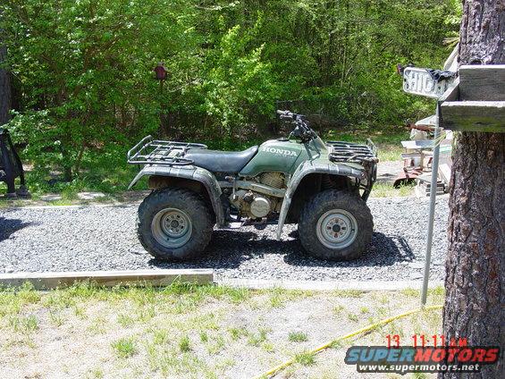 Green four-wheeler ATV parked on gravel, side view