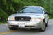 2004 Ford Crown Victoria - A silver 2004 Ford Crown Victoria is shown from the front on a paved road with trees lining the background.