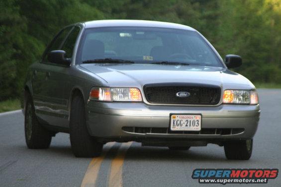 Silver 2004 Ford Crown Victoria on a road with trees in the background. License plate KGC-2103