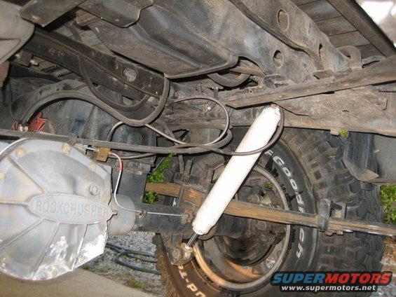 Undercarriage of a vehicle showing a "Rockcrusher" differential cover, white shock absorber, and leaf springs