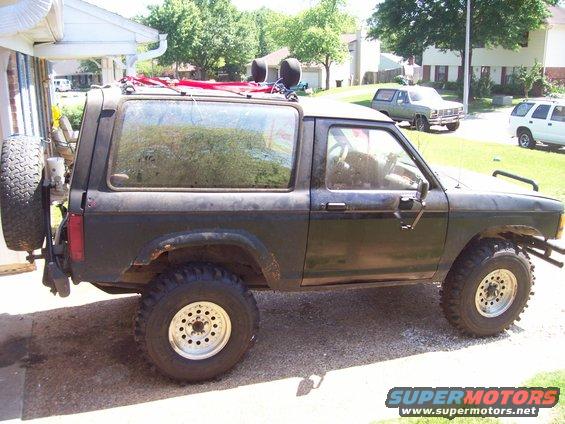 Dark green 1989 Ford Bronco II parked outside a house with a spare tire on the back and roof rack