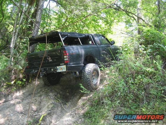 Black pickup truck with off-road tires and a soft top, driving on a dirt trail