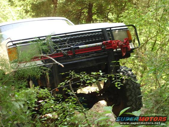White 1989 Ford Bronco with red Hi-Lift jack on front bumper, navigating rough terrain