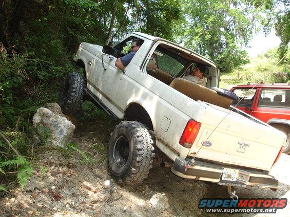 White Ford Bronco climbing a rocky hill with a red Jeep behind it