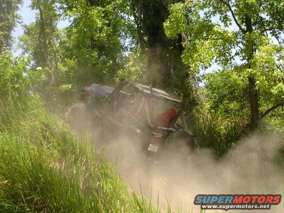 Off-road vehicle with roll cage kicking up dust on a grassy incline