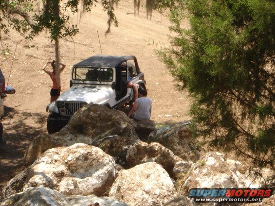 White Jeep Wrangler with black top parked on rocky terrain with people around