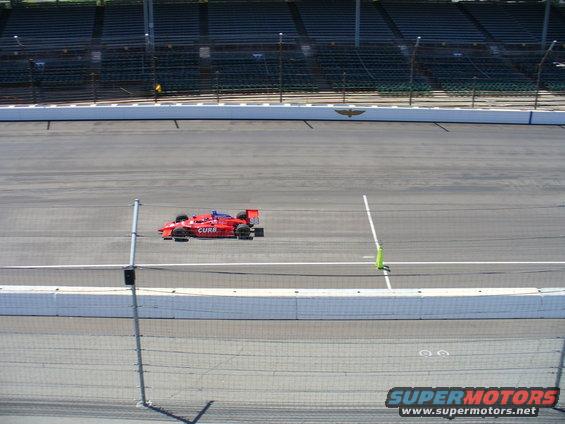 Red open-wheel race car on a track, with grandstands in the background