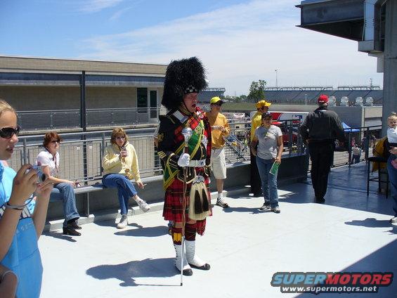 People gathered on a deck overlooking a race track, one person in Scottish Highland dress